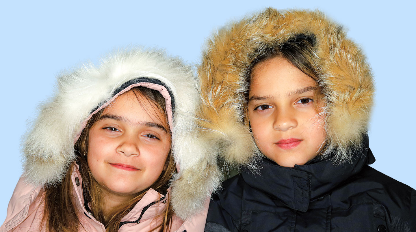 Two young kids smile and wear winter jackets.