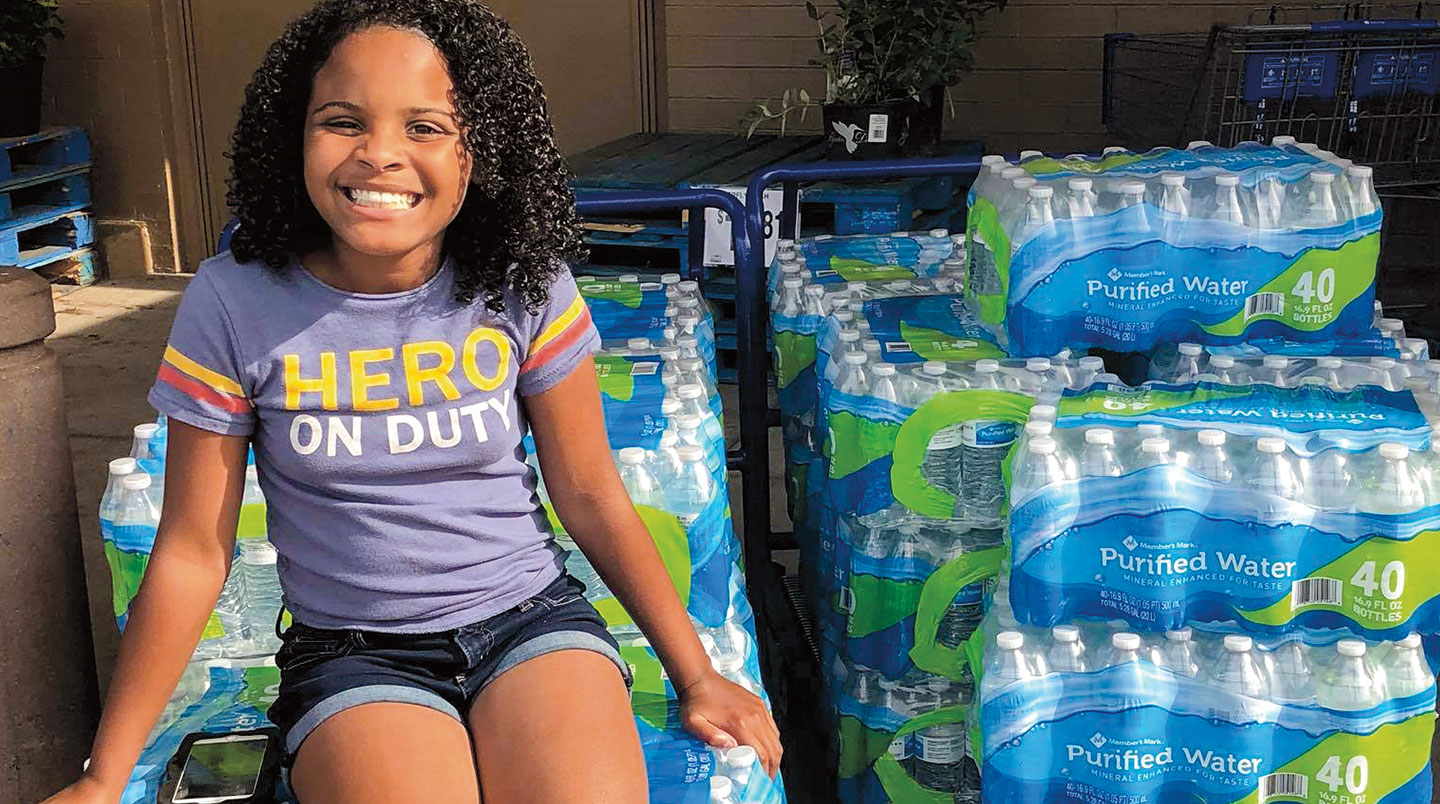 Mari Copeny smiles while sitting atop a stack of plastic water bottles.