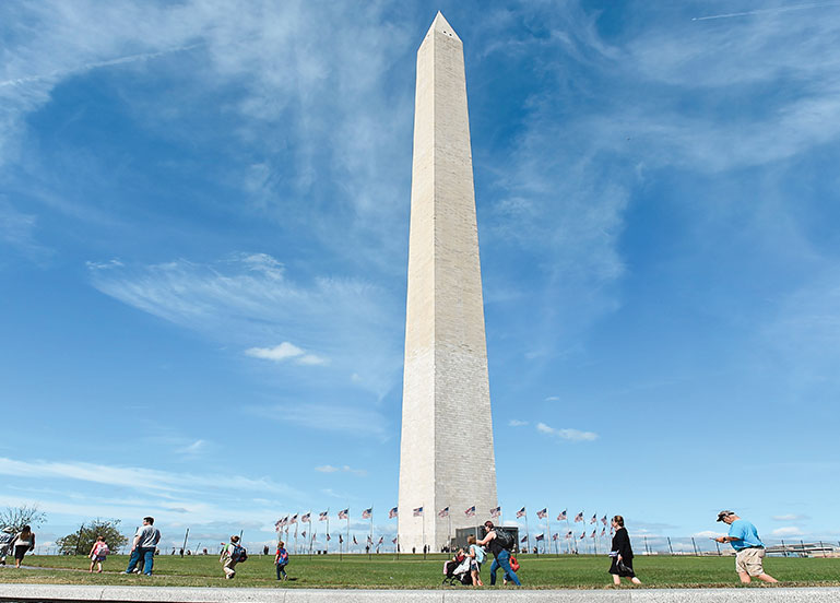 The Washington Monument is a tall light-colored obelisk surrounded by a circle of American flags.