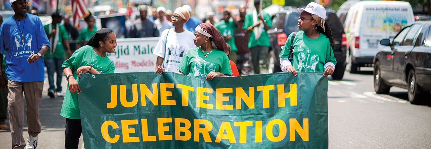 Kids carry a Juneteenth Celebration banner during a parade.