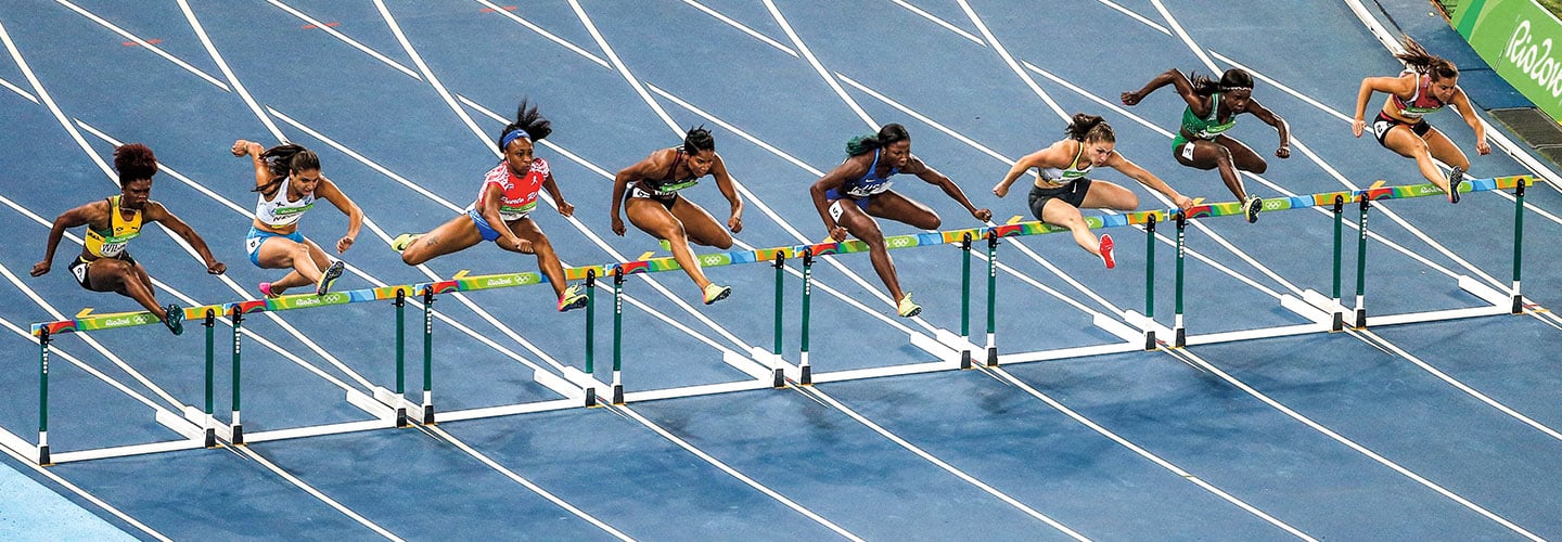 Female Olympic runners leap over hurdles.