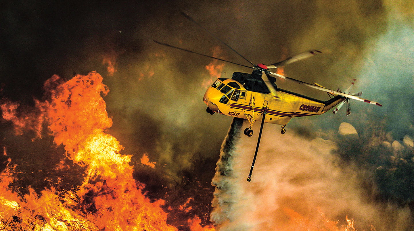 A helicopter drops water over a fire.