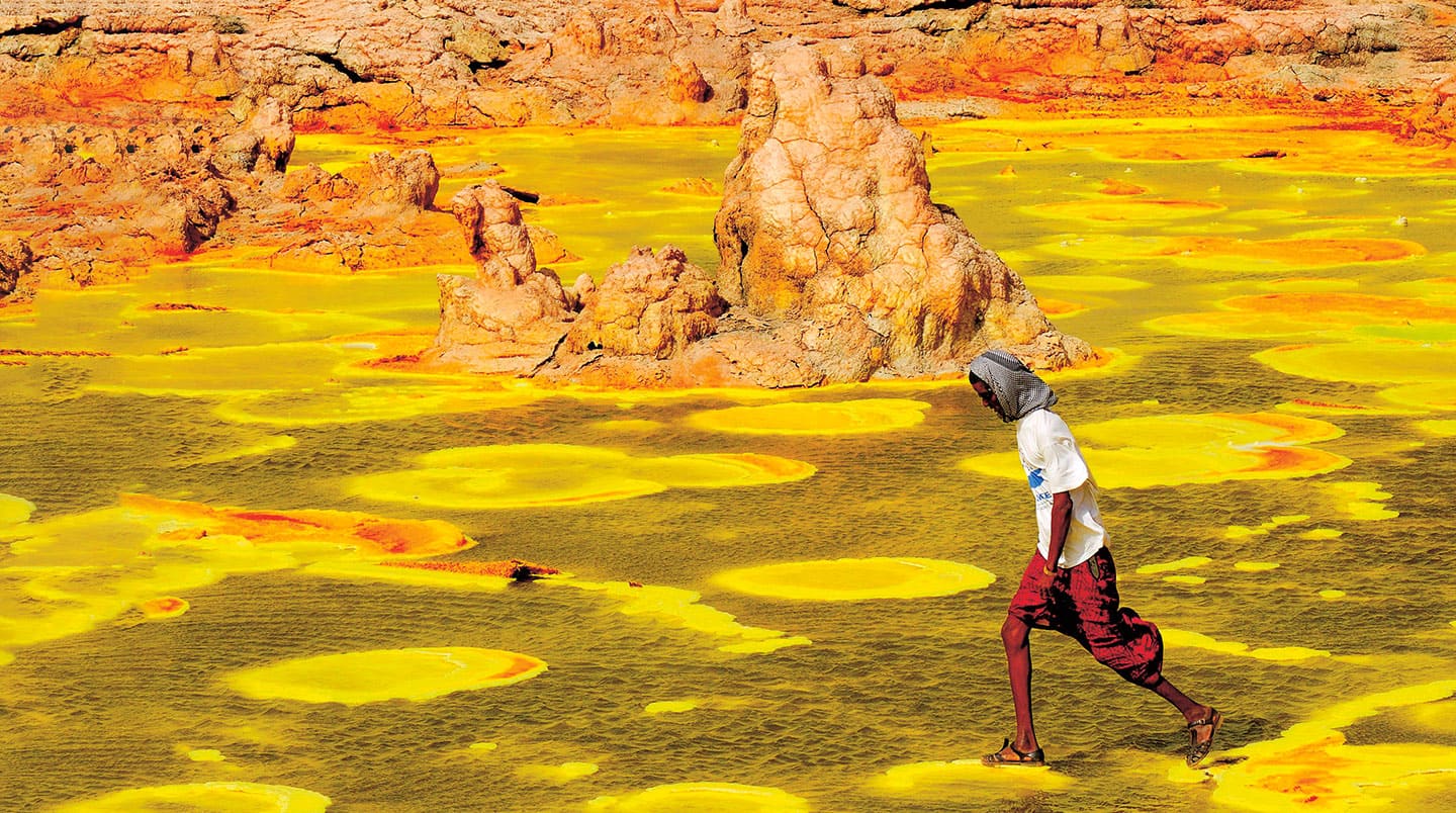 A man walks across a brightly colored salt flat.