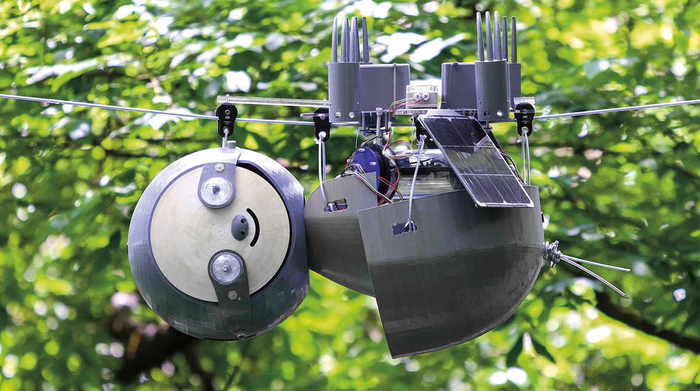 A robot with a smiley face hangs from a wire.