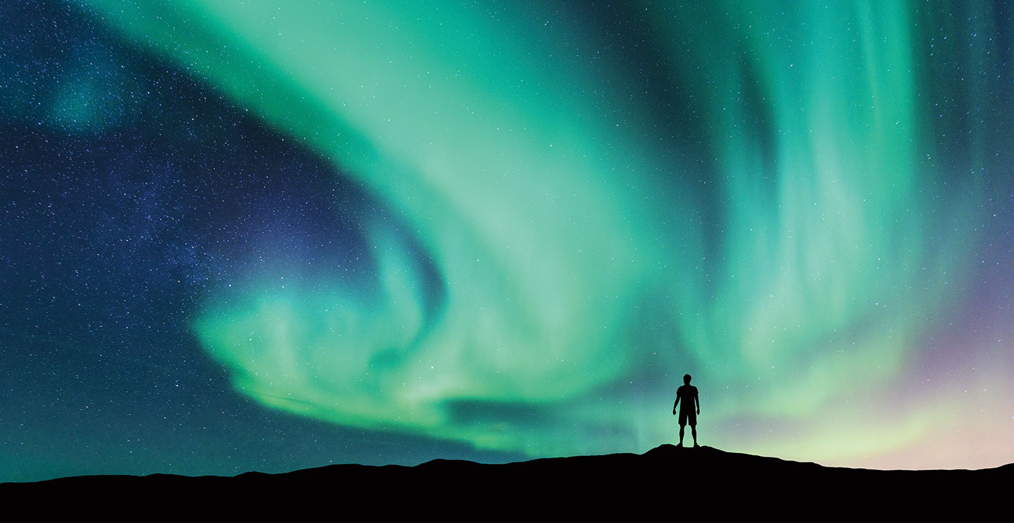 A person watches the swirling colors of the Northern lights in the sky.