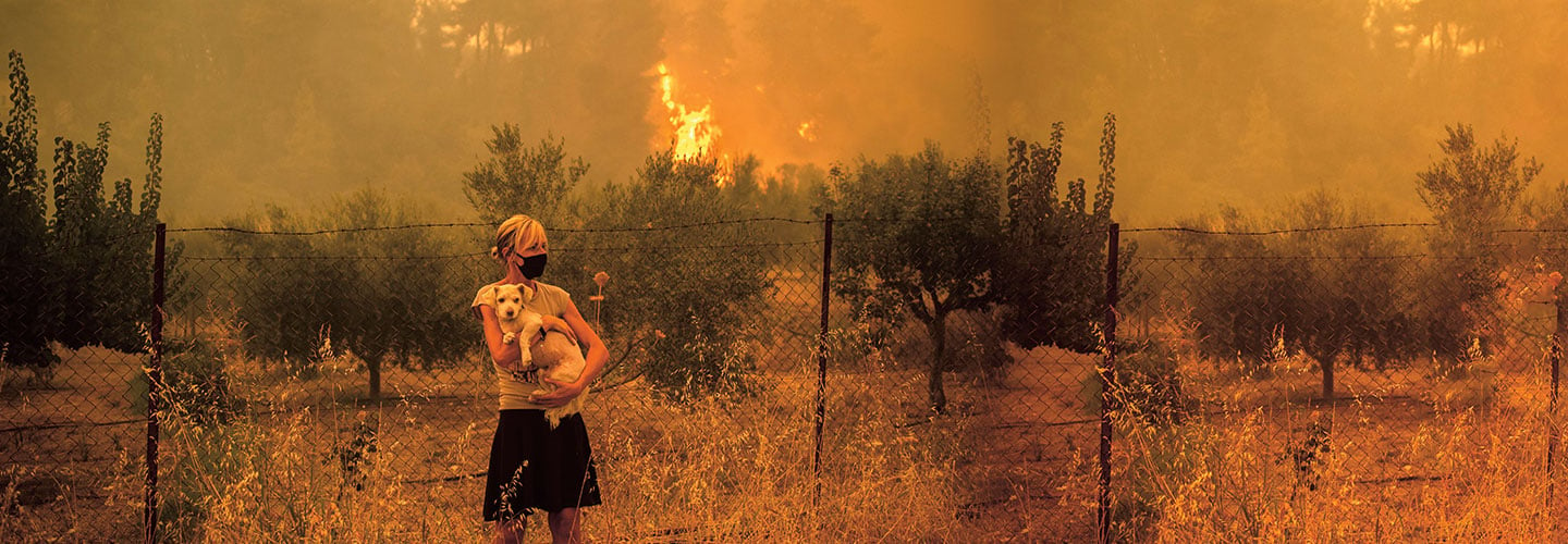 Woman holding her dog away from a wildfire.
