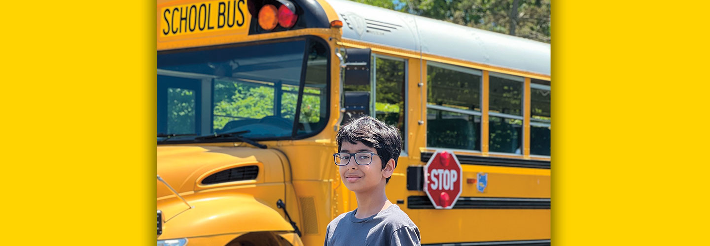 Student posing in front of a school bus