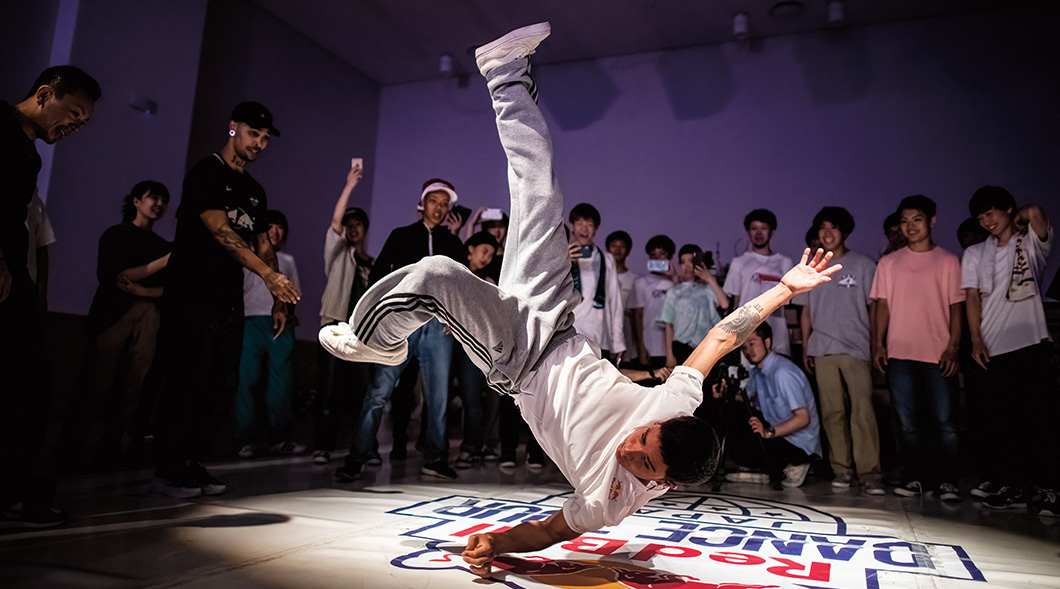 Image of a person break dancing in front of a gathered crowd