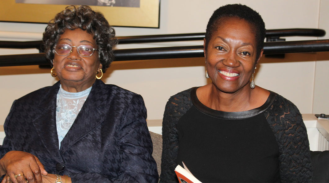 Two women smile at the camera, one in a black jacket and one in a black lace-sleeved top