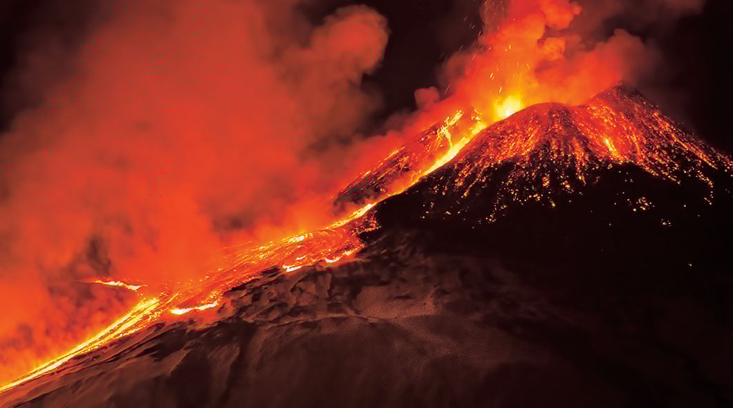 Volcano erupting with glowing lava flowing down its slopes and ash clouds rising into the night sky