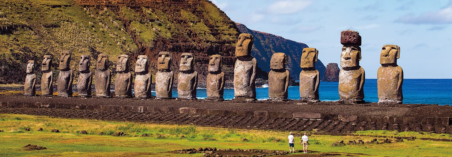 A row of moai statues on Easter Island with two people standing at their base