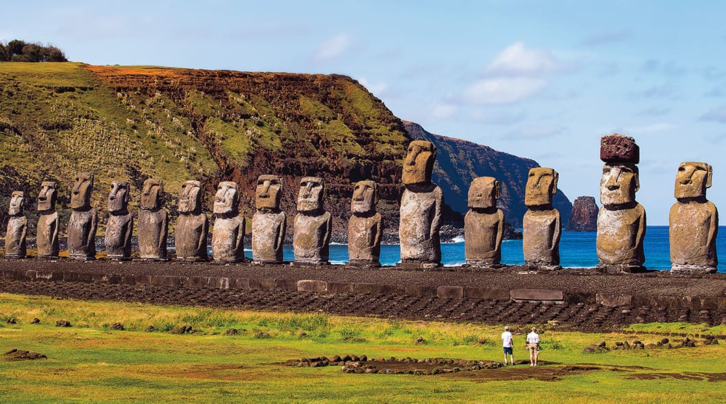 A row of moai statues on Easter Island with two people standing nearby for scale