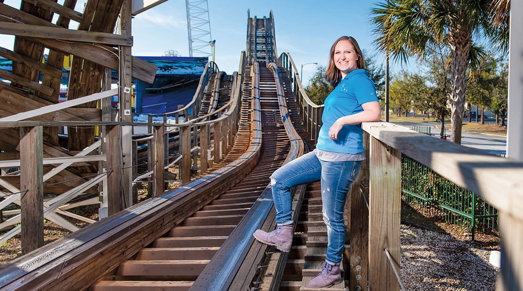 A woman stands on the wooden track structure of a roller coaster at an amusement park